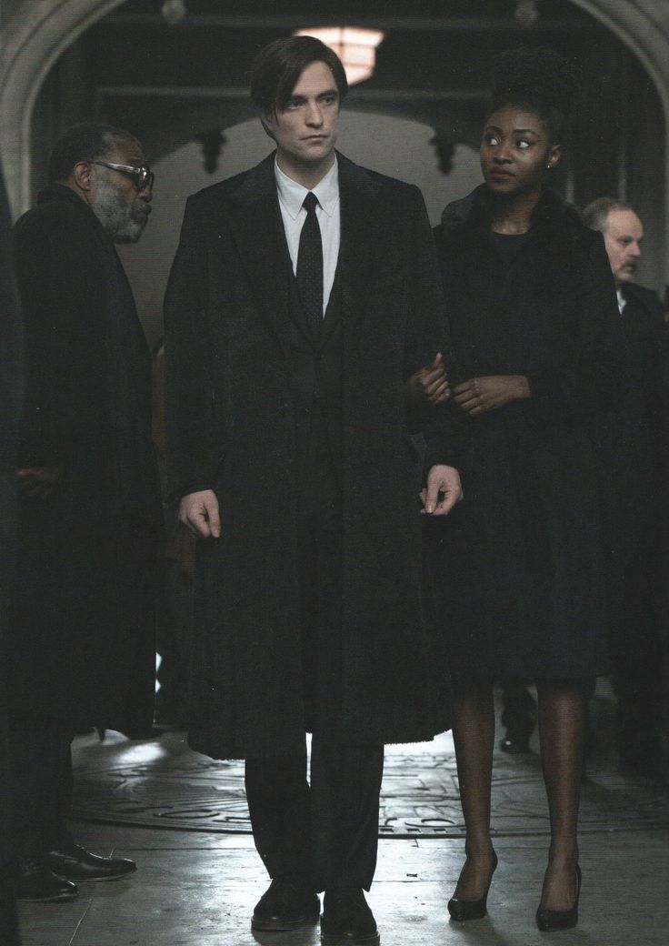 a man in a long coat and tie standing next to other people wearing black coats