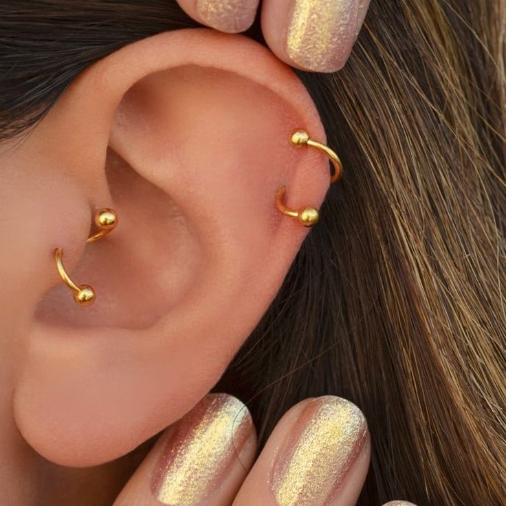 a woman's ear with gold colored nail polishes and piercings on it