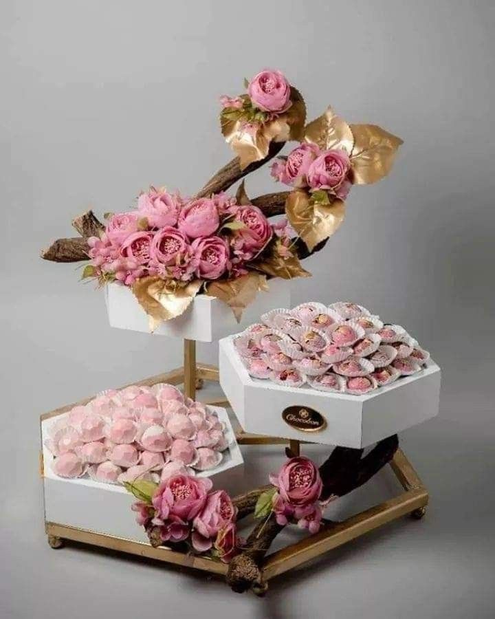 three white boxes filled with pink flowers on top of a wooden stand next to each other