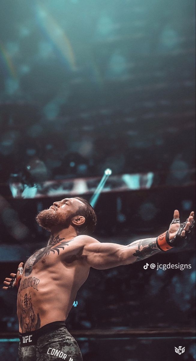 a man with tattoos on his arm standing in the middle of a wrestling ring