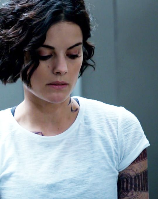 a woman with tattoos looking down at her cell phone while wearing a white t - shirt