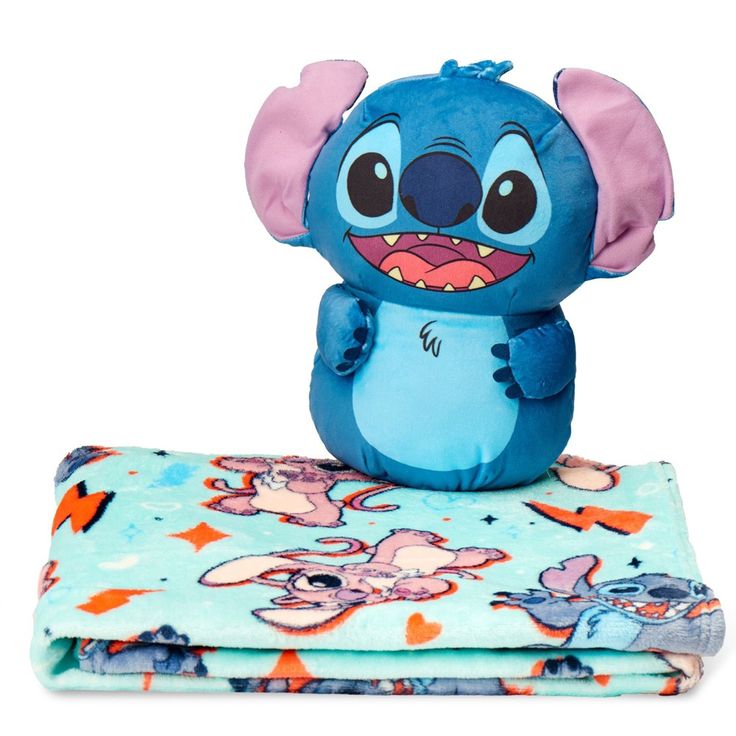 a blue stuffed animal sitting on top of a blanket next to two blankets with cartoon characters