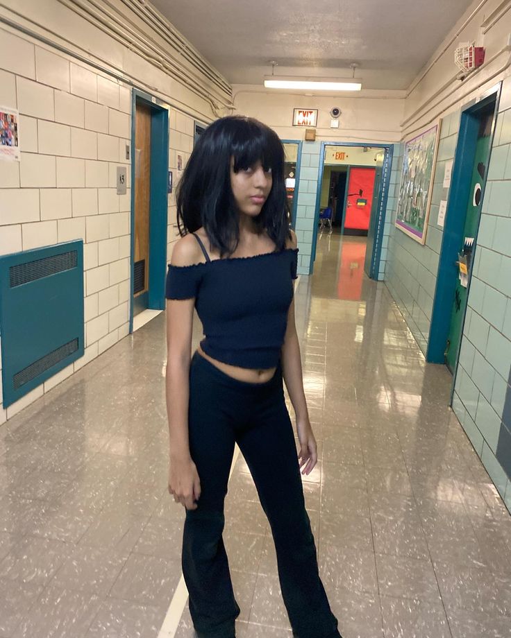 a woman standing in the middle of a hallway wearing black pants and cropped top