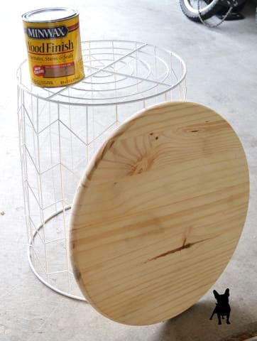 a wooden object sitting on the ground next to a wire rack with paint in it