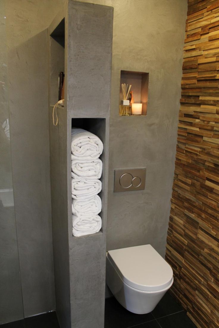 a bathroom with a toilet and some towels on the shelf next to it in front of a stone wall