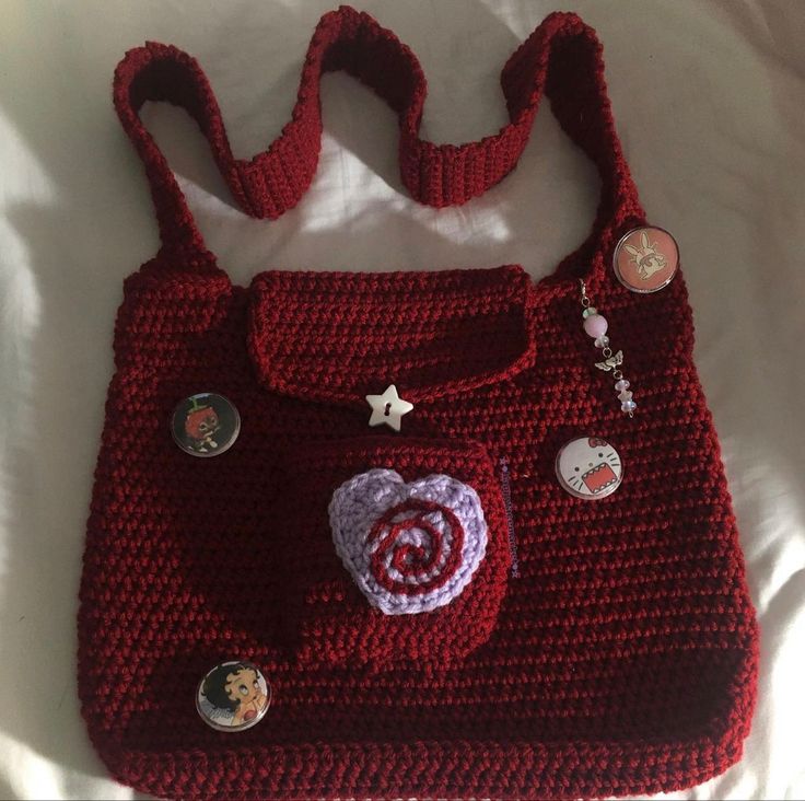 a crocheted red purse with buttons and a heart on the front, sitting on a bed