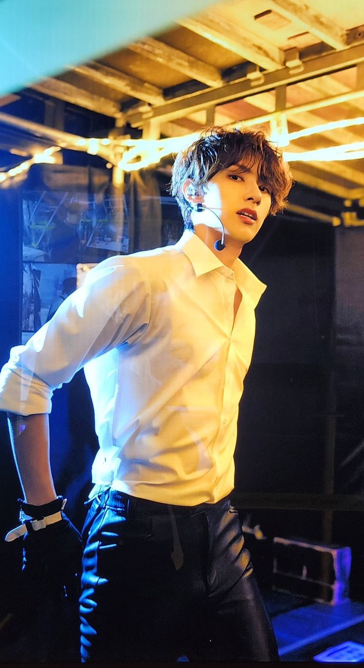 a young man in white shirt and black pants standing next to a blue light with his hands on his hips