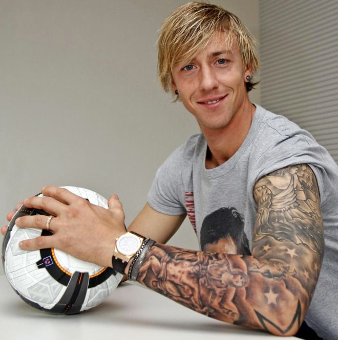 a man sitting at a table with a soccer ball in his hand and tattoos on his arm