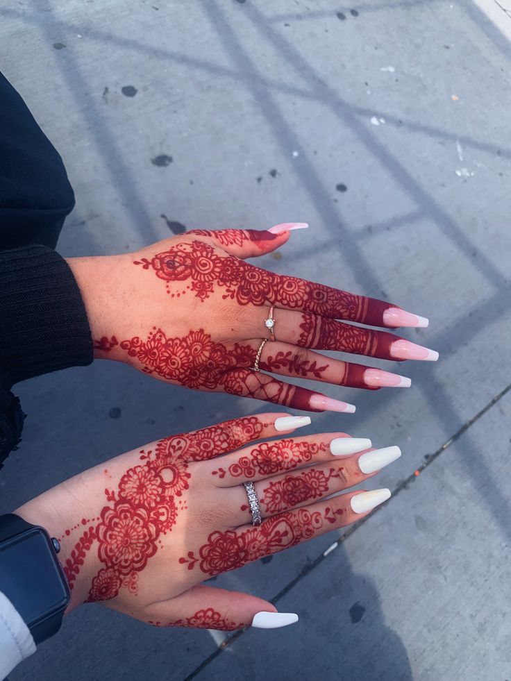 two hands with red henna on them and one hand with white nails holding a ring