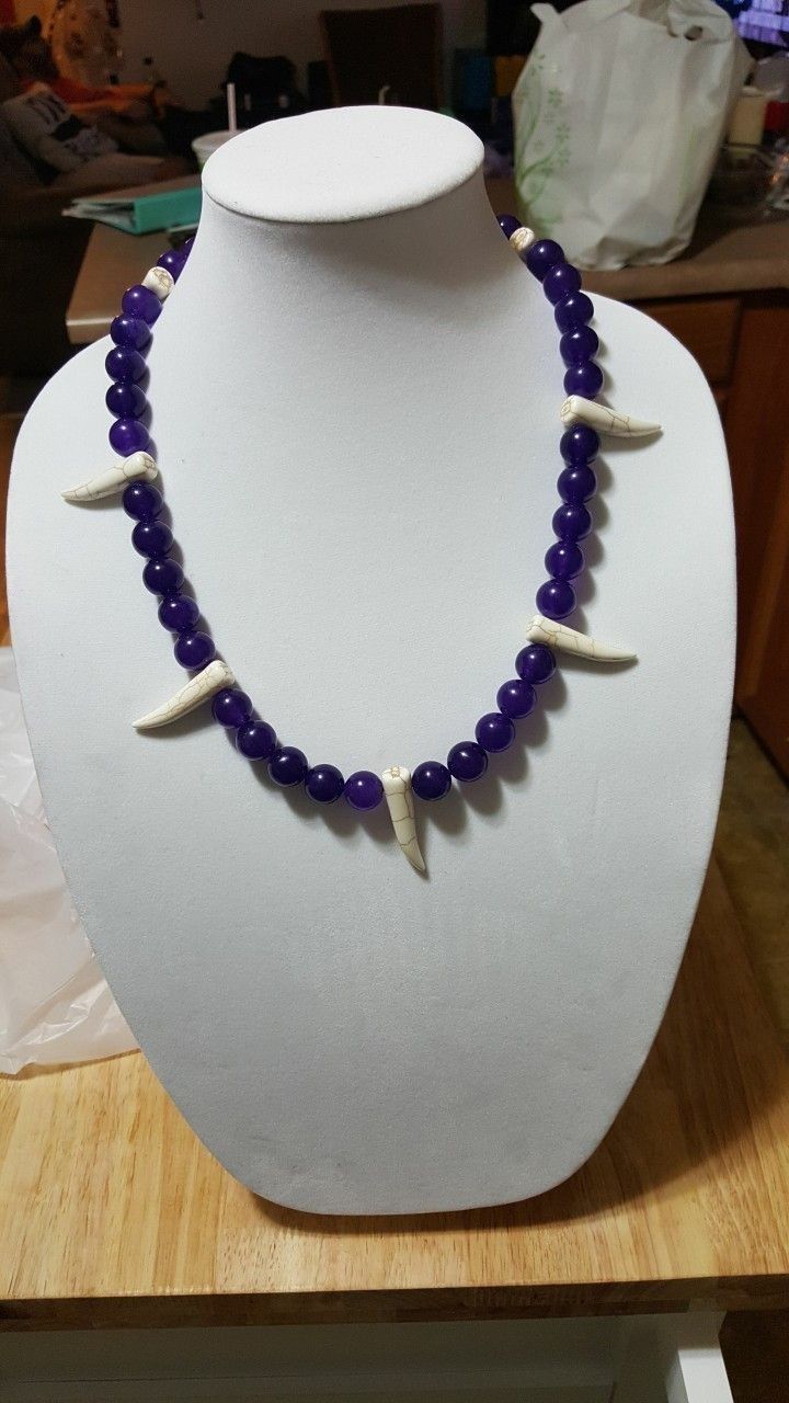 a necklace is on display on a white mannequin with purple beads and shells