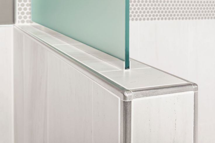 the corner of a white tiled bathroom with a green glass partition on it's side