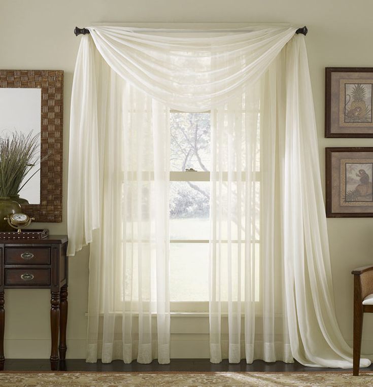 a white curtain hanging in front of a window next to a wooden table and chair