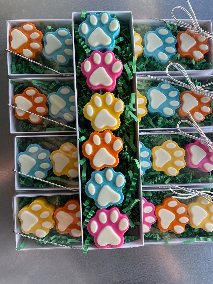 a box filled with lots of different colored dog paw cookies on top of green grass