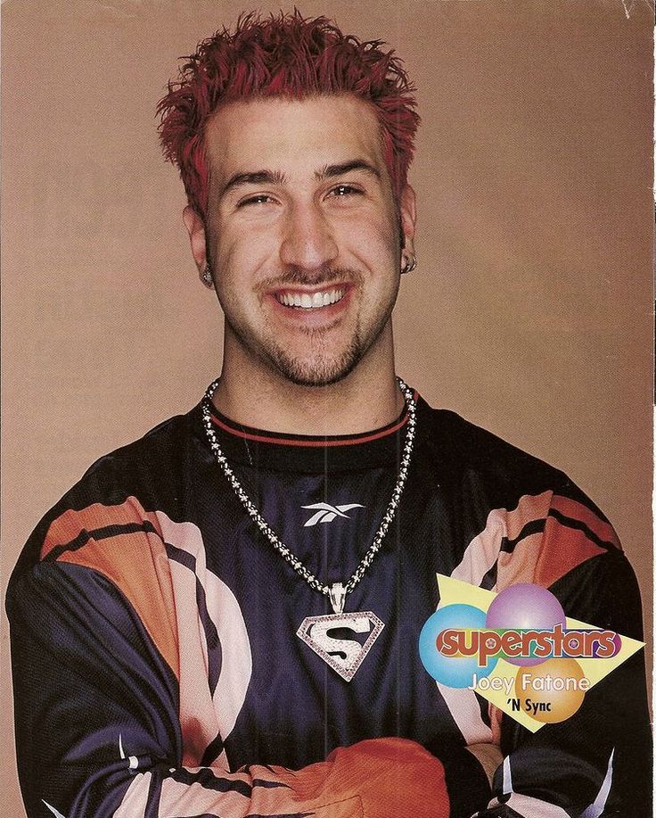 a man with red hair wearing a black shirt and silver necklace smiling at the camera