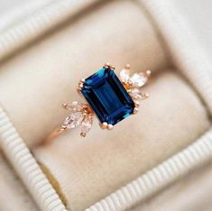 an engagement ring with a blue stone surrounded by small white and clear stones in a box