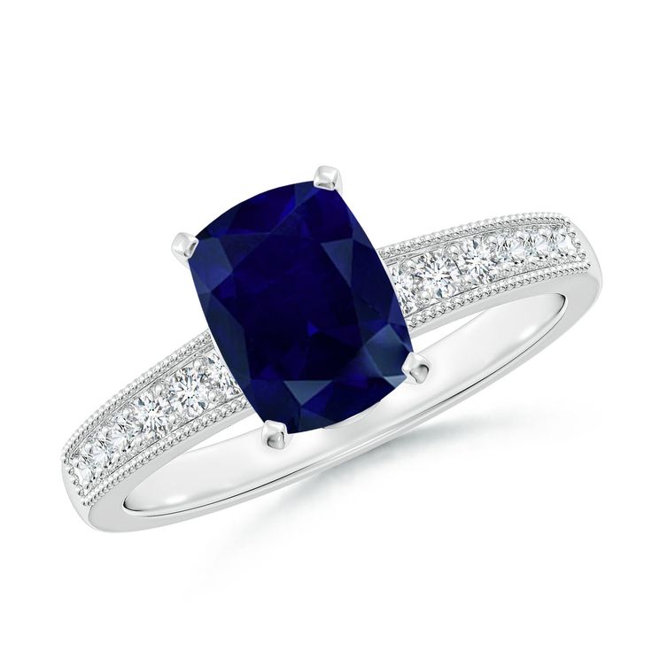 a cushion shaped blue sapphire and diamond ring with shoulder accents on the band, set in 18k white gold