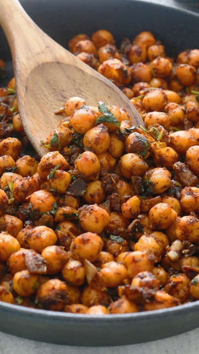 a wooden spoon in a pan filled with cooked chickpeas and herbs on the side