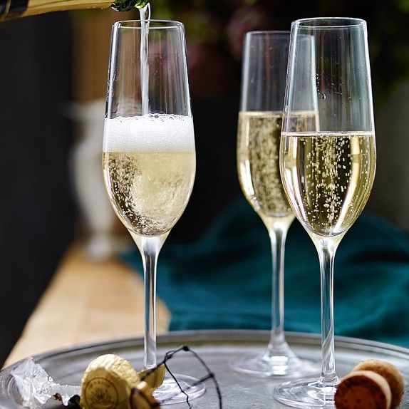 champagne being poured into wine glasses on top of a silver tray with crackers and shells