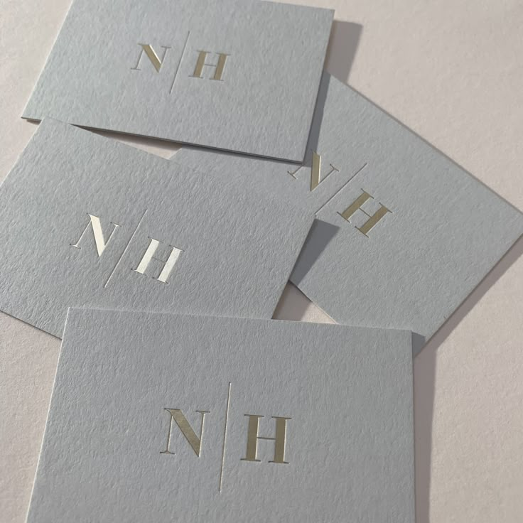 four business cards with the letter n and h in gold foil on grey card stock