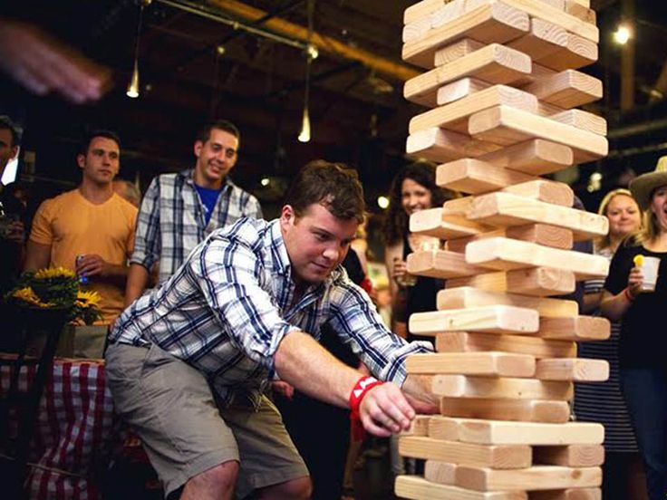 a group of people standing around a giant stack of wooden blocks in front of a man