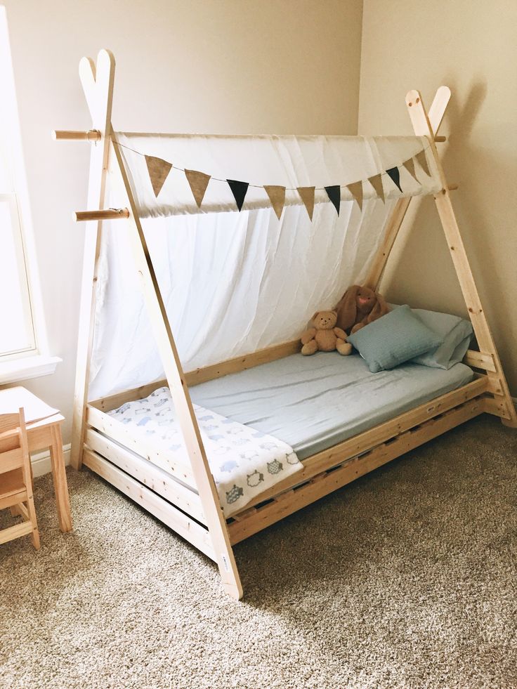 a child's bed made out of wood with a canopy over it and stuffed animals on the floor