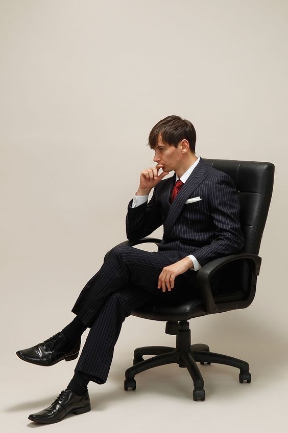 a man in a suit and tie sitting on a chair with his hand to his chin