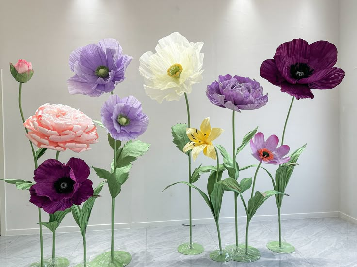 four vases filled with different colored flowers on top of a marble floor in front of a white wall