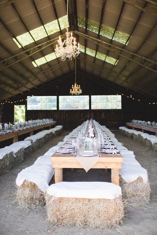 a barn with hay bales and tables set up for a dinner party in the middle