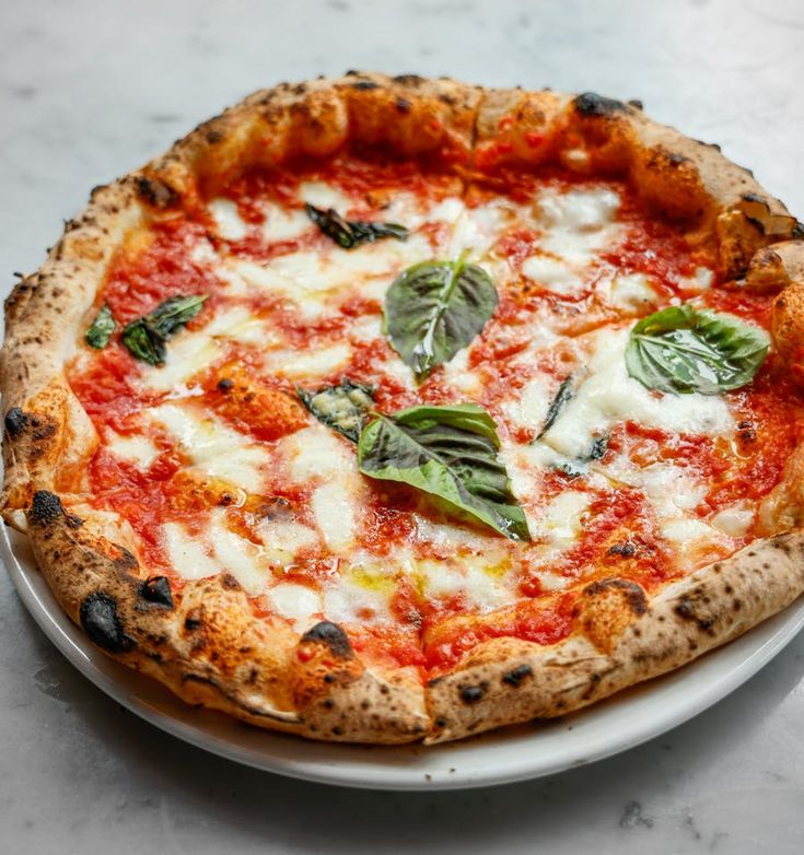 a close up of a pizza on a plate with cheese and basil leaf toppings