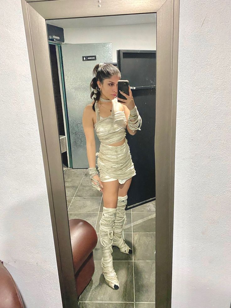 a woman in short skirt and boots taking a selfie with her cell phone while standing in front of a mirror