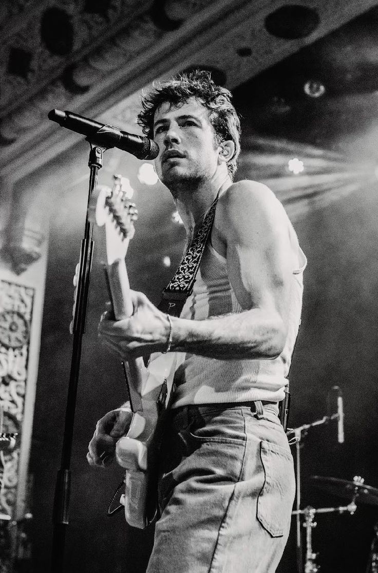 a shirtless man holding a guitar while standing in front of a microphone on stage