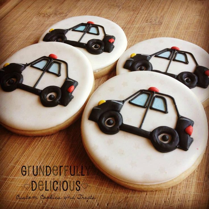 four decorated cookies sitting on top of a wooden table with white frosting and black icing