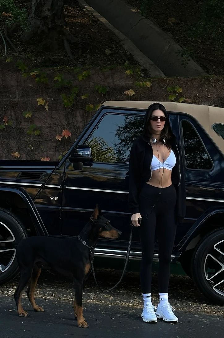 a woman in white bra top and black pants standing next to a dog on leash