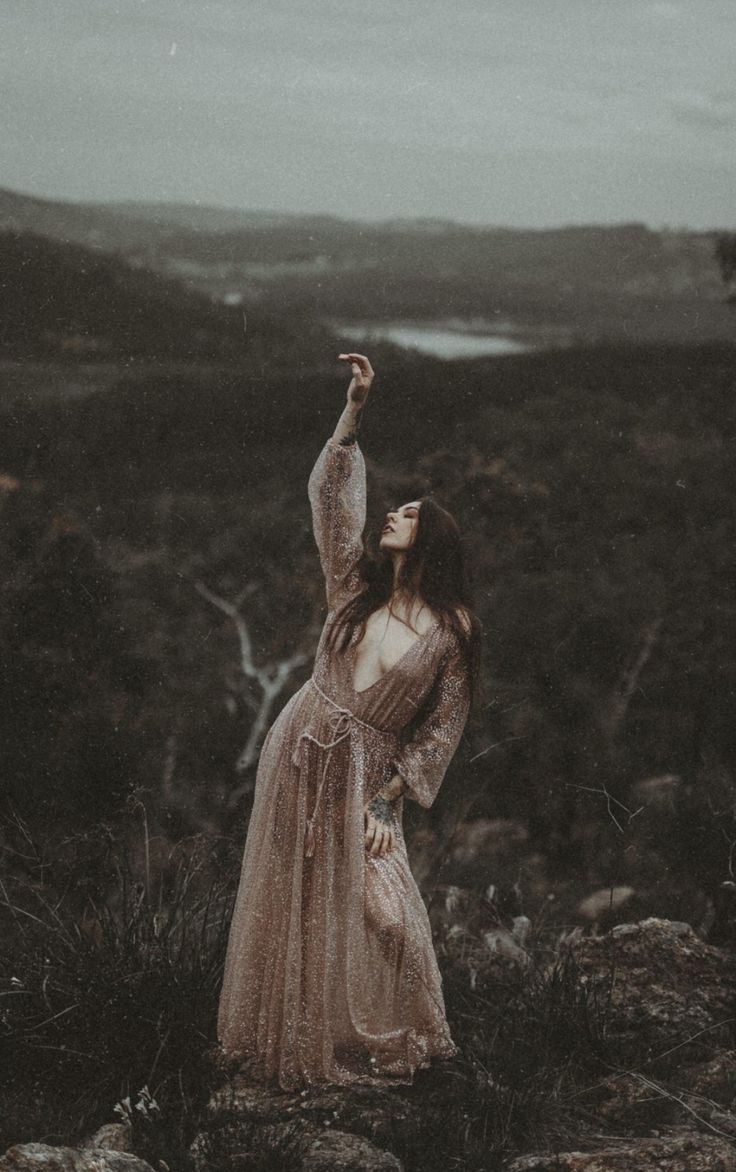 a woman in a long dress standing on top of a rocky hill with her arms up