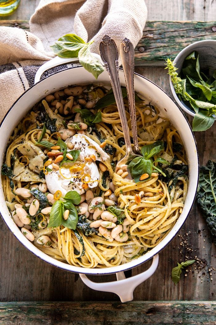 a pot filled with pasta, beans and spinach on top of a wooden table