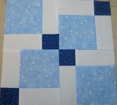 a blue and white patchwork quilt is laying on top of a tablecloth that has been cut into squares