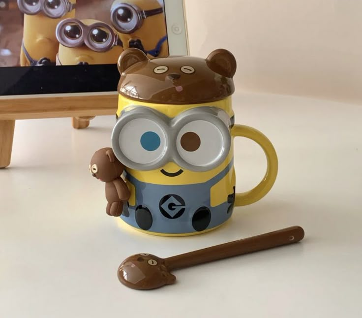 a yellow and blue minion mug sitting on top of a table next to a spoon