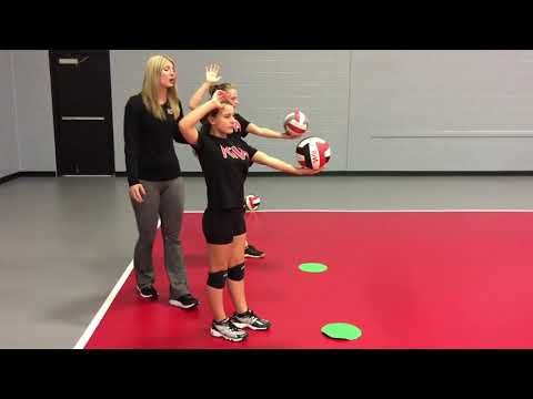 two women in black shirts and shorts playing with green frisbees on a gym floor