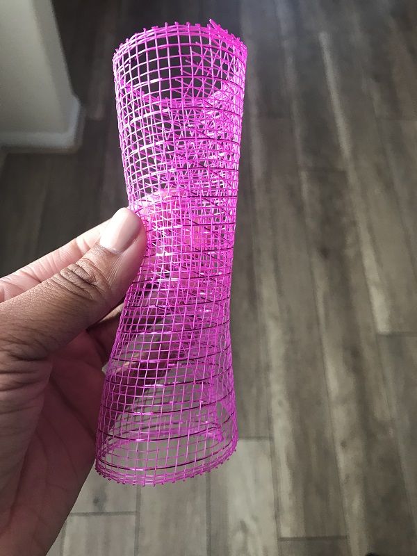 a hand holding a pink piece of wire on top of a wooden floor next to a wall