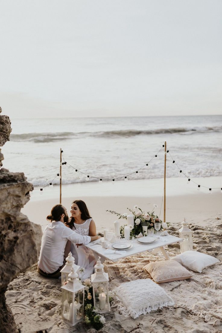 two people sitting at a table on the beach