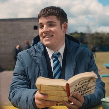 a man sitting at a table with an open book in his hands and smiling for the camera