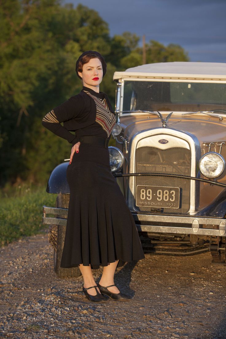 a woman standing in front of an old car