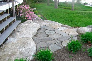 a stone path in the middle of a yard with steps leading up to it and flowers on either side