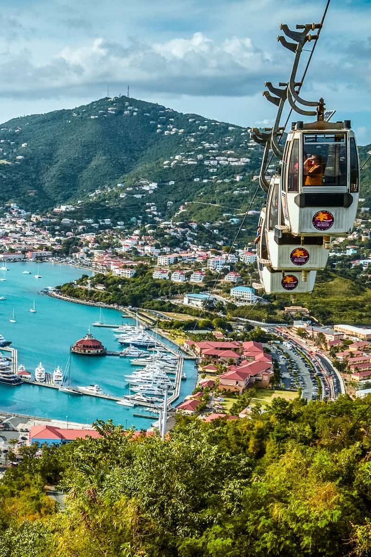 a cable car going over the water with boats docked in the bay and mountains in the background