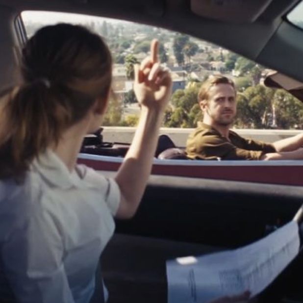 two people sitting in the back seat of a car and one person pointing at something