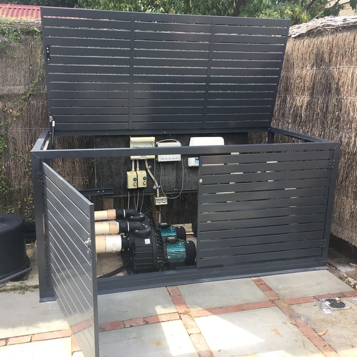 an open metal box sitting on top of a brick floor next to a fence and trees