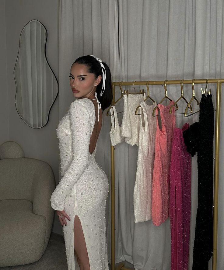 a woman in a white dress standing next to a rack with dresses on hangers