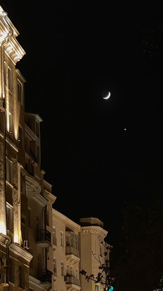 the moon is visible in the night sky over some buildings