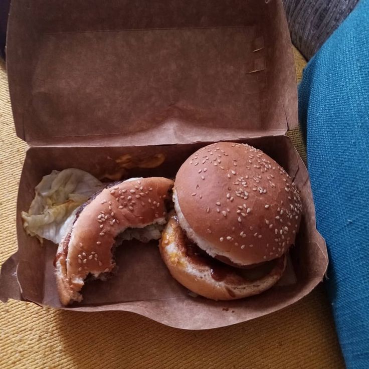 two hamburgers sitting in a brown paper container on a table next to a blue chair