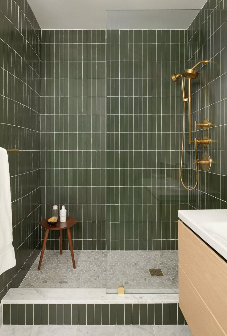 a green tiled bathroom with a wooden stool and shower head next to the bathtub